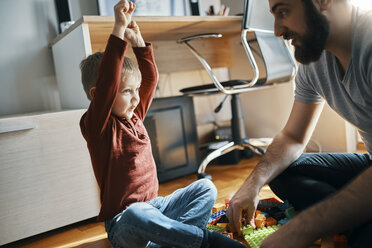 Vater und Sohn sitzen zu Hause auf dem Boden und spielen zusammen mit Bauklötzen - ZEDF01279