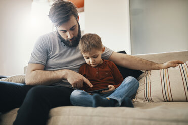 Father and little son sitting together on the couch looking at smartphone - ZEDF01293