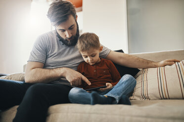 Vater und kleiner Sohn sitzen zusammen auf der Couch und schauen auf ihr Smartphone - ZEDF01293