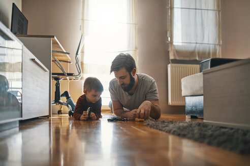 Father and son lying together on the floor playing with toy cars - ZEDF01296