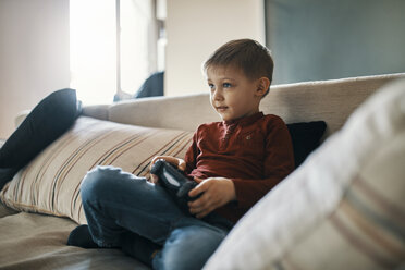 Portrait of little boy sitting on the couch playing computer game - ZEDF01297