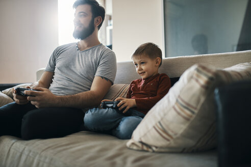 Father and son sitting together on the couch playing computer game - ZEDF01299