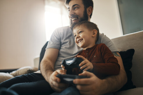 Glücklicher Vater und kleiner Sohn sitzen zusammen auf der Couch und spielen ein Computerspiel - ZEDF01300