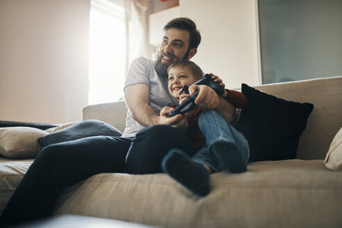 Father and son sitting together on the couch playing computer game - ZEDF01301