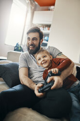 Lachender Vater und kleiner Sohn sitzen zusammen auf der Couch und spielen ein Computerspiel - ZEDF01303