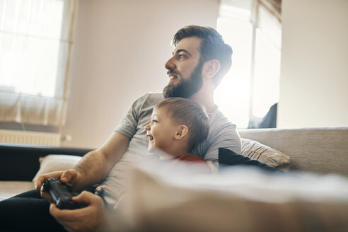 Father and son sitting together on the couch playing computer game - ZEDF01304