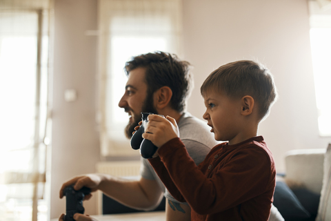 Kleiner Junge spielt mit seinem Vater zu Hause ein Computerspiel, lizenzfreies Stockfoto