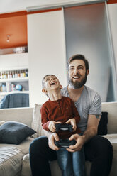 Father and son sitting together on the couch playing computer game - ZEDF01307