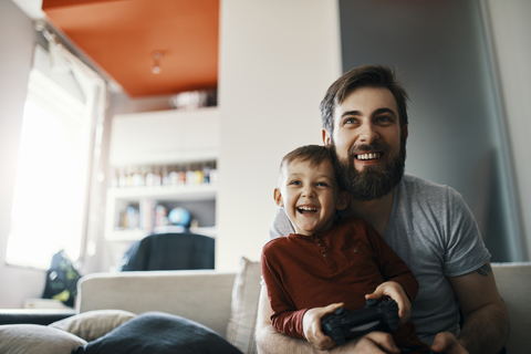 Father and son sitting together on the couch playing computer game stock photo