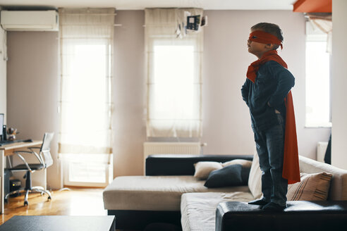 Little boy dressed up as a superhero standing on coffee table at home - ZEDF01313