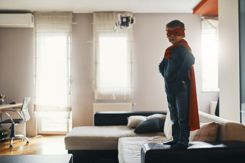 Little boy dressed up as a superhero standing on coffee table at home - ZEDF01314