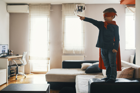 Little boy dressed up as a superhero standing on coffee table at home pointing on something stock photo