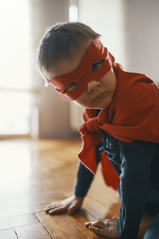 Little boy dressed up as a superhero crouching on the floor at home stock photo