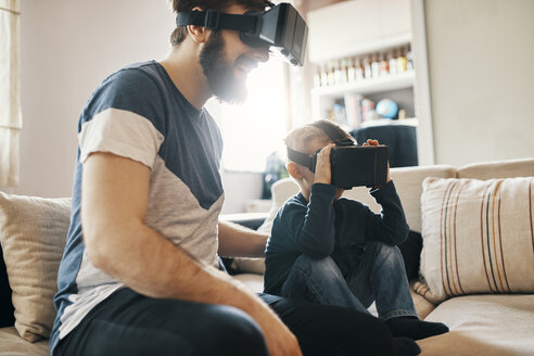 Father and little son sitting on the couch at home wearing virtual reality glasses - ZEDF01327