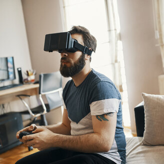 Man wearing virtual reality glasses at home playing computer game - ZEDF01328