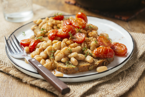 White bean and tomato ragout on toast, white beans, vegetable bouillon powder, Italian herbs, whole grain toast, cherry tomatoes, thyme stock photo