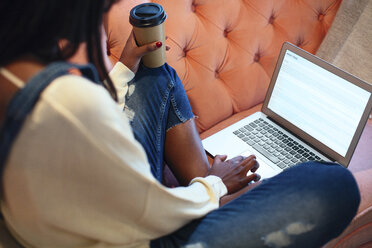 Junge Frau auf der Couch sitzend mit Kaffee zum Mitnehmen und Laptop - EBSF02324