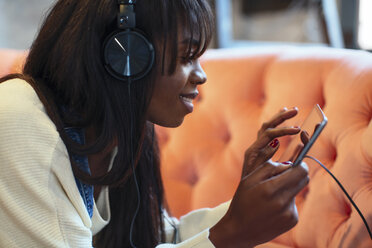 Smiling young woman on the couch using tablet and headphones - EBSF02335