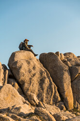 Italy, Sardinia, hiker with hat and backpack resting on a rock - AFVF00405