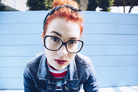 Porträt einer rothaarigen jungen Frau mit Brille, die auf einer Bank sitzt, lizenzfreies Stockfoto