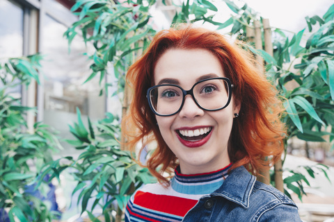 Porträt einer lächelnden rothaarigen jungen Frau vor einer Pflanze, lizenzfreies Stockfoto