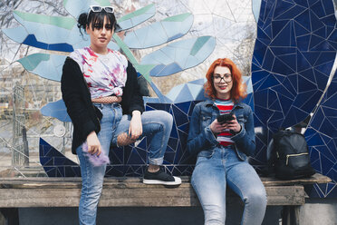 Porträt von Hipster-Freundinnen, die Handys vor einer Mosaikwand halten - MASF01369