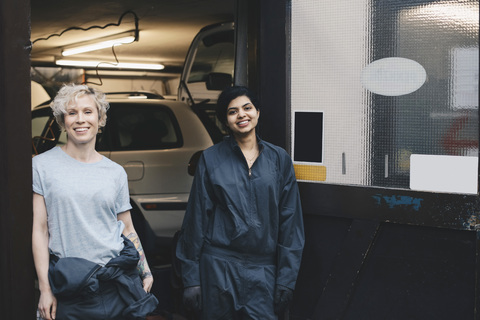Porträt einer lächelnden Mechanikerin, die am Eingang einer Autowerkstatt steht, lizenzfreies Stockfoto