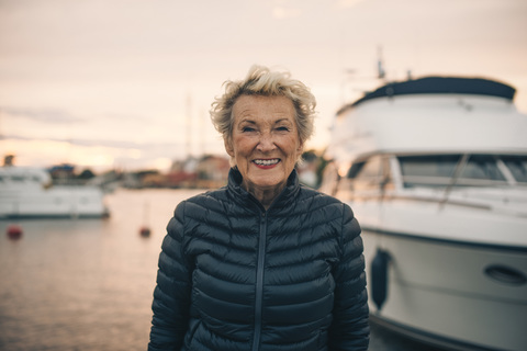 Porträt einer glücklichen älteren Frau, die bei Sonnenuntergang am Hafen steht, lizenzfreies Stockfoto