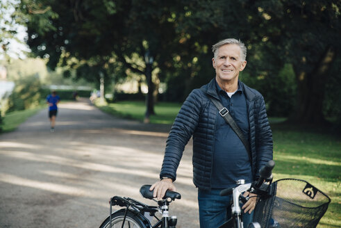 Porträt eines lächelnden älteren Mannes mit Fahrrad, der im Park steht - MASF01439
