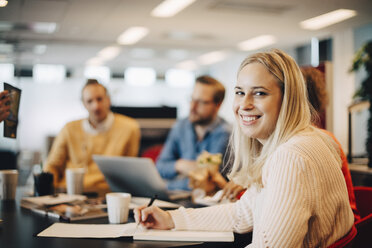 Portrait of smiling young businesswoman sitting with colleagues at conference table in office - MASF01441