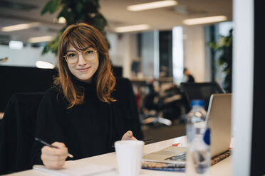 Portrait of confident young businesswoman holding pen while sitting at desk in office - MASF01442