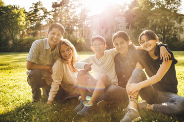 Porträt einer lächelnden Familie, die auf einer Wiese im Park sitzt - MASF01445