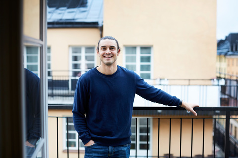 Porträt eines lächelnden jungen Mannes auf dem Balkon einer Mietwohnung, lizenzfreies Stockfoto