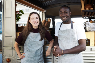 Portrait of smiling male and female owners standing outside food truck parked in city - MASF01452