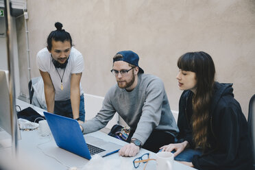 Multi-ethnic male and female computer programmers using laptop at desk in office - MASF01474