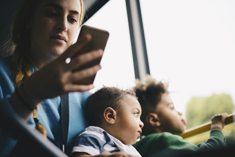 Mutter benutzt Mobiltelefon, während sie mit ihrem Sohn im Bus sitzt, lizenzfreies Stockfoto