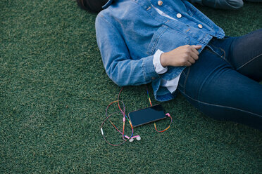 Midsection of teenage girl lying by mobile phone on grass - MASF01485