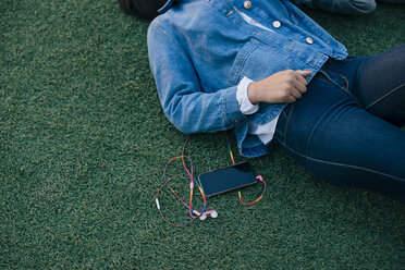 Mittelteil eines Teenagers, der mit seinem Handy im Gras liegt - MASF01485