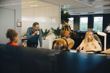 Multi-ethnic colleagues discussing at office seen from glass - MASF01505