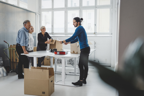 Multiethnische Geschäftsleute packen Kartons in ihrem neuen Büro aus, lizenzfreies Stockfoto