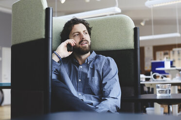Mittlerer Erwachsener, männlicher Fachmann, der über sein Smartphone spricht, während er auf einem Stuhl im Kreativbüro sitzt - MASF01540