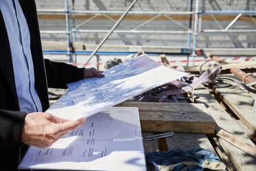 Midsection of architect with blueprint on table at construction site - MASF01545