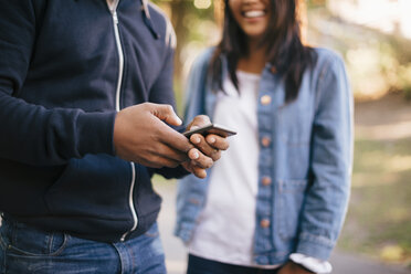 Mittelteil eines Mannes, der ein Mobiltelefon benutzt, während er neben einer Freundin steht - MASF01548