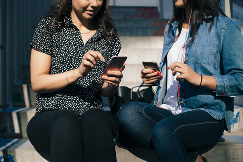 Mittelteil von Freundinnen, die Smartphones benutzen, während sie auf einer Treppe sitzen - MASF01550