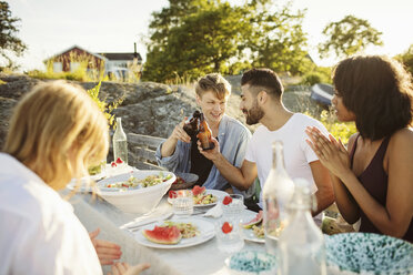 Men toasting beer bottles while sitting with friends at picnic table - MASF01568