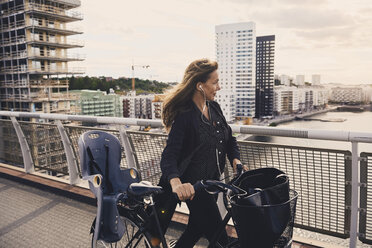 Ältere Frau zu Fuß mit Fahrrad auf einer Fußgängerbrücke in der Stadt - MASF01574