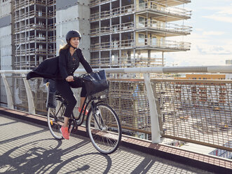 Mature woman cycling on footbridge against building - MASF01577