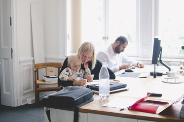 Mid adult businesswoman with baby girl working at table in creative office - MASF01579