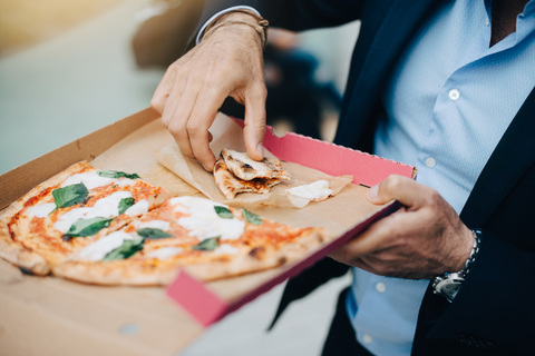 Mittelteil eines Geschäftsmannes, der in der Stadt eine Pizza aus einem Karton isst, lizenzfreies Stockfoto