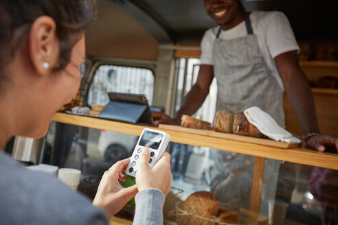 Mid adult woman using credit card reader to pay salesman at food truck - MASF01609